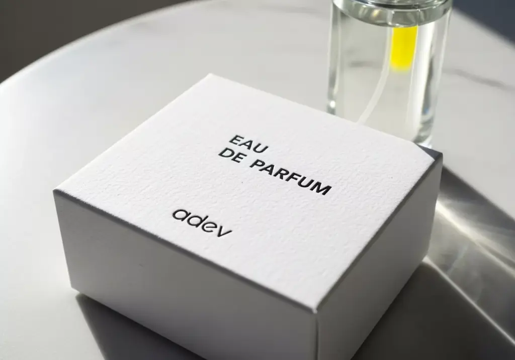 Contoh kemasan parfum minimalis berwarna putih dengan teknik blind emboss dan tipografi sederhana.